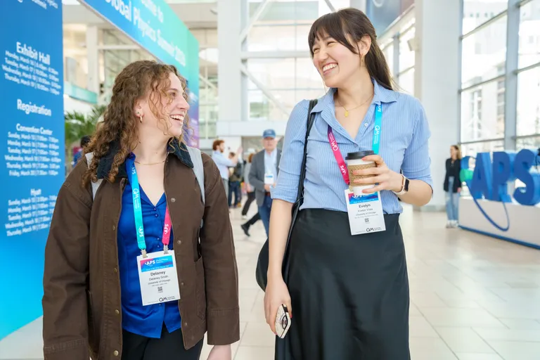 Two women attendees share a laugh as they walk at meeting.
